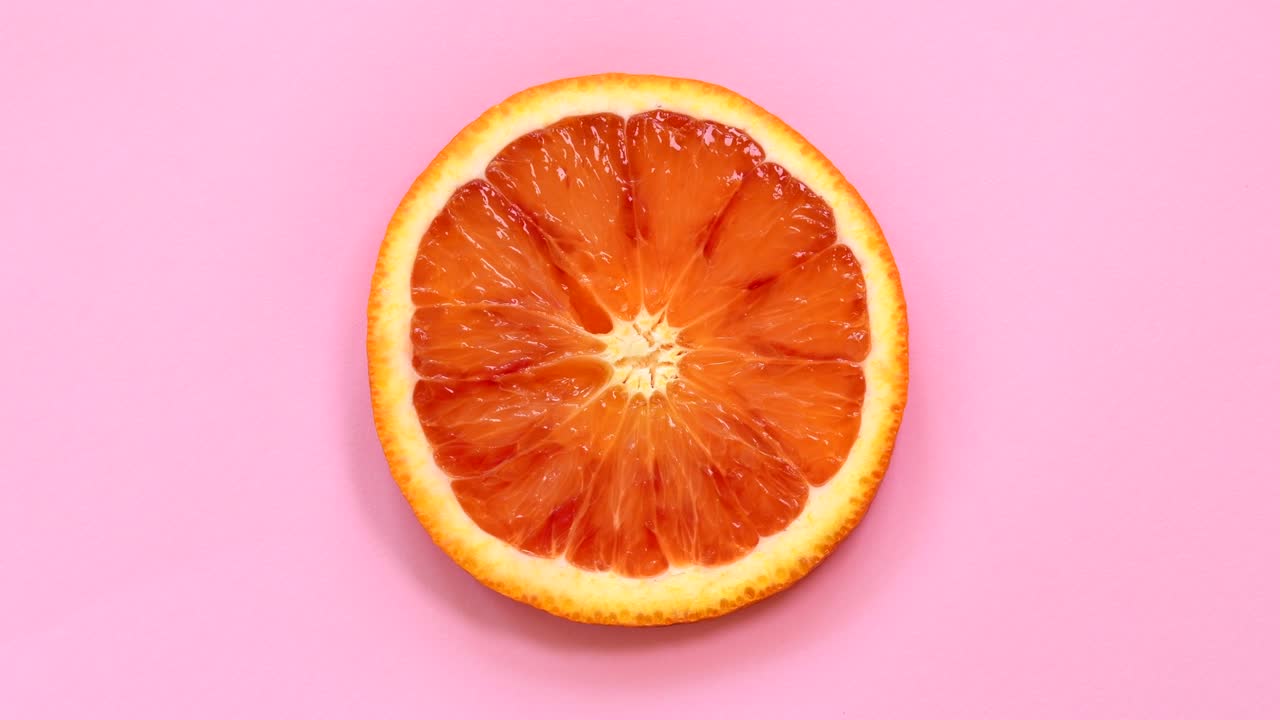Fetta di arancia rossa che ruota vista dall'alto su sfondo rosa