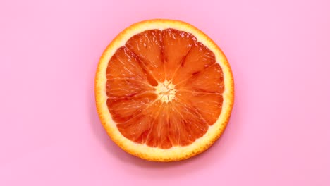 una rebanada de naranja de sangre girando en la vista superior sobre un fondo rosado