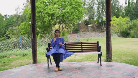 Ein-Asiatisches-Mädchen-Im-Park,-Das-Allein-Auf-Einer-Bank-Sitzt-Und-Telefoniert