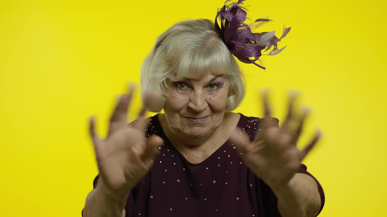 Anziana donna amichevole che saluta con la mano guardando la telecamera con un sorriso smagliante, dicendo ciao, salutando