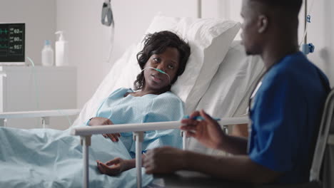 a black male doctor is talking to a black female patient lying on a hospital bed and connected to an acid supply. the attending physician discusses with the patient in the hospital the treatment