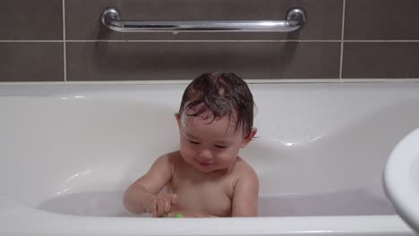 cheerful happy toddler baby girl happily playing alone with plastic toy while bathing in the bathtub at home bathroom