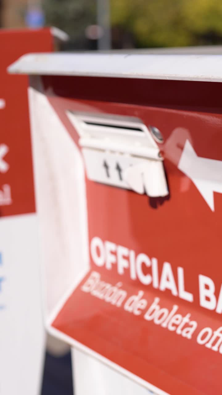 Young Man Deposits Mail-In Ballot Letter into Official Ballot Box Next to Drop Ballot Here Sign Vertical