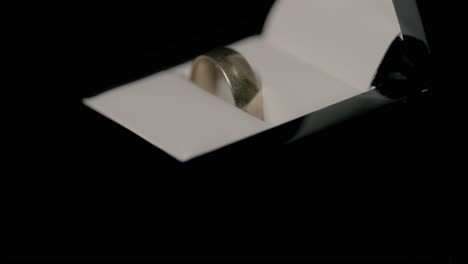 a stunning engagement ring in an elegant box slowly spins against a dark background, illuminated by soft, focused lighting