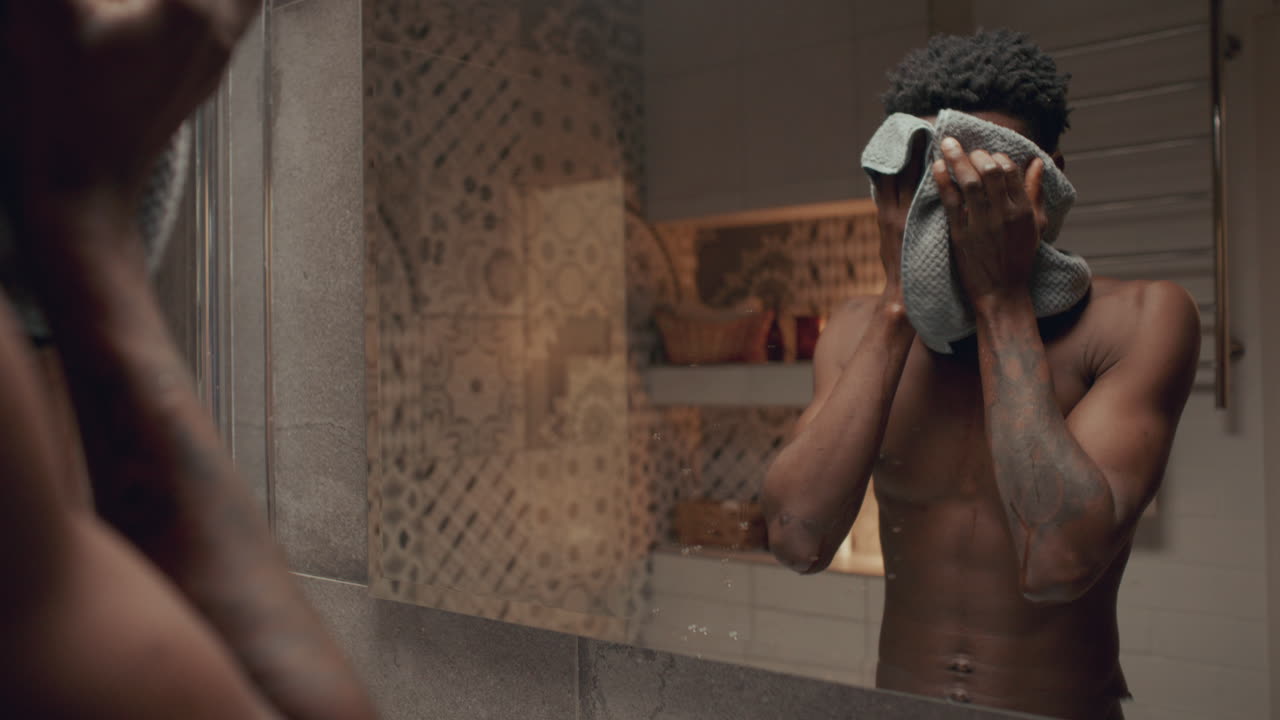 joven negro lavándose la cara y mirándose en el espejo del baño