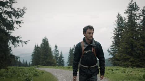 gimbal shot of ahiker walking on a macadam road looking in left and right direction to admire the nature, wearing a windproof jacket