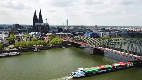 drone shot of a cargo boat crossing under the bridge in cologne (köln) with the city as the backdrop scenery, germany.