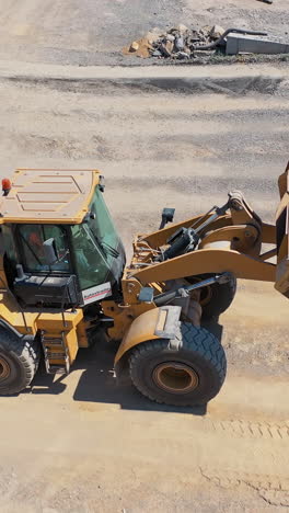 excavator on the territory of asphalt manufacture outdoors. modern excavator pouring out sand from bucket into a special tank. top view. vertical video