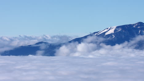 칠레의 칼부코 화산을 보여주는 낮은 구름 위의 시간 경과, 화산에 눈, 밝은 푸른 하늘을 보여줍니다.