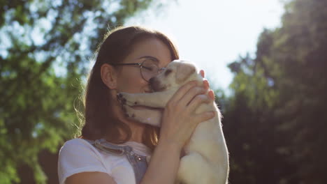 Kaukasische-Junge-Frau-Mit-Brille,-Die-An-Einem-Sommertag-Einen-Labrador-Welpen-Im-Park-Hält-Und-Küsst