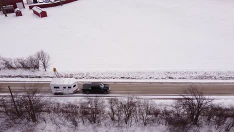 Transporting-horses-in-white-trailer-on-winter-rural-road,-aerial-drone-shot