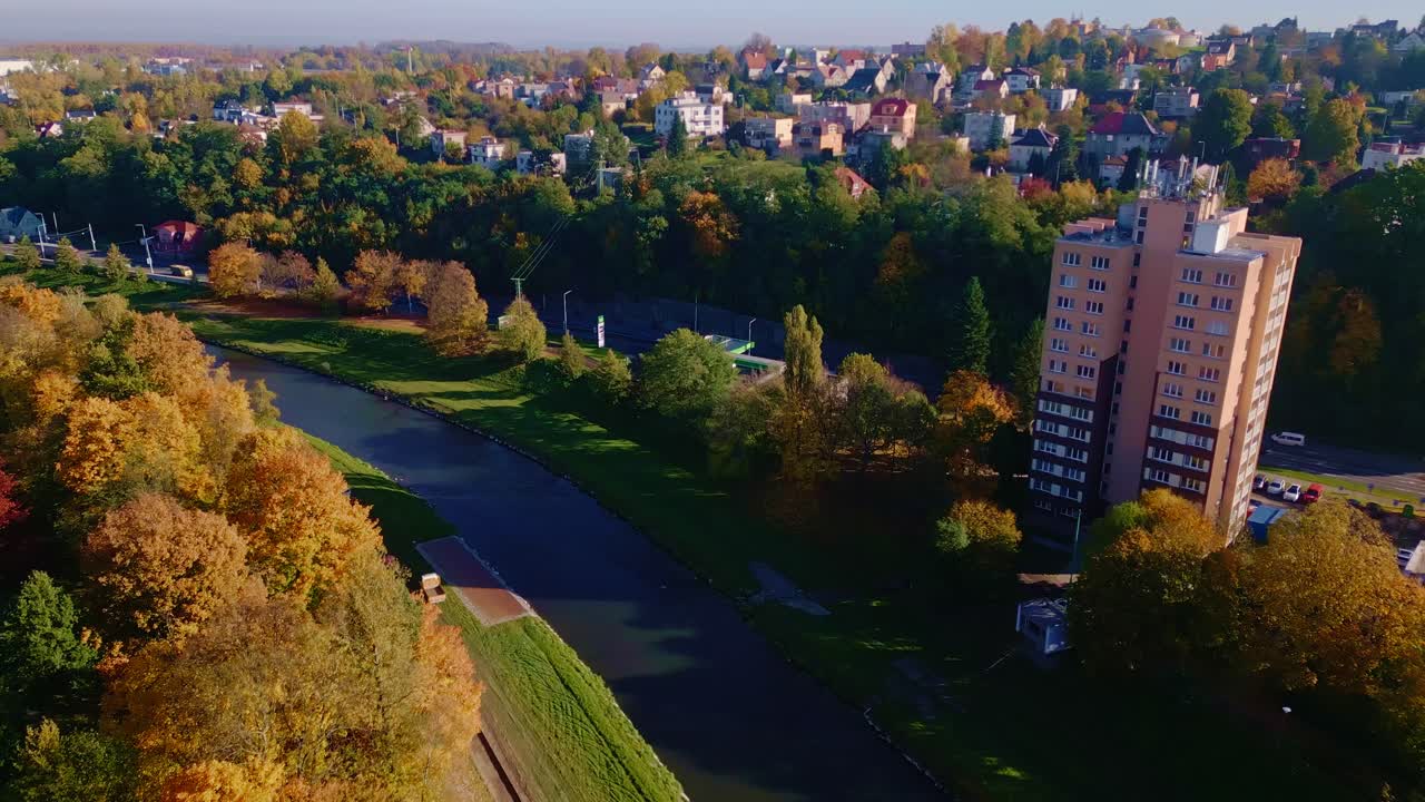 Drone flight over river to urban scene amid colourful Autumnal trees