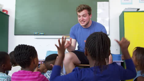 elementary school kids sitting on floor playing with teacher