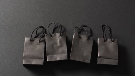 four black gift bags with black handles in a row on dark grey background with copy space