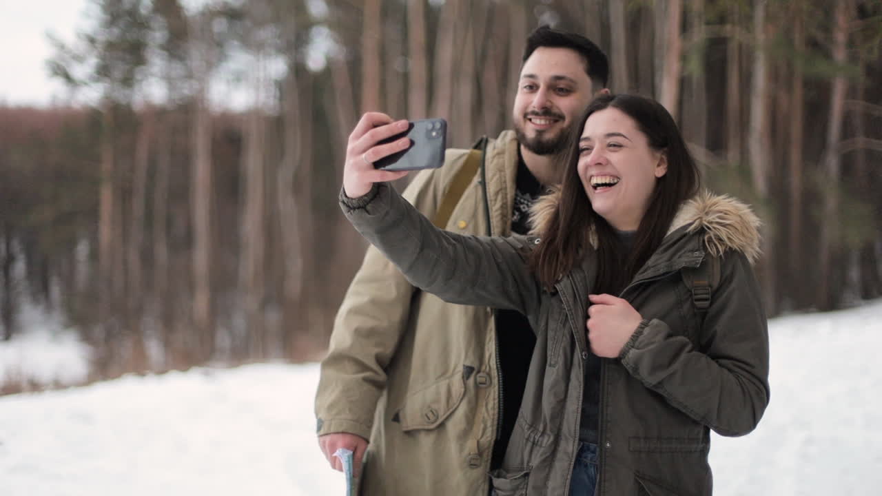 pareja caucásica tomando selfies en un bosque nevado.