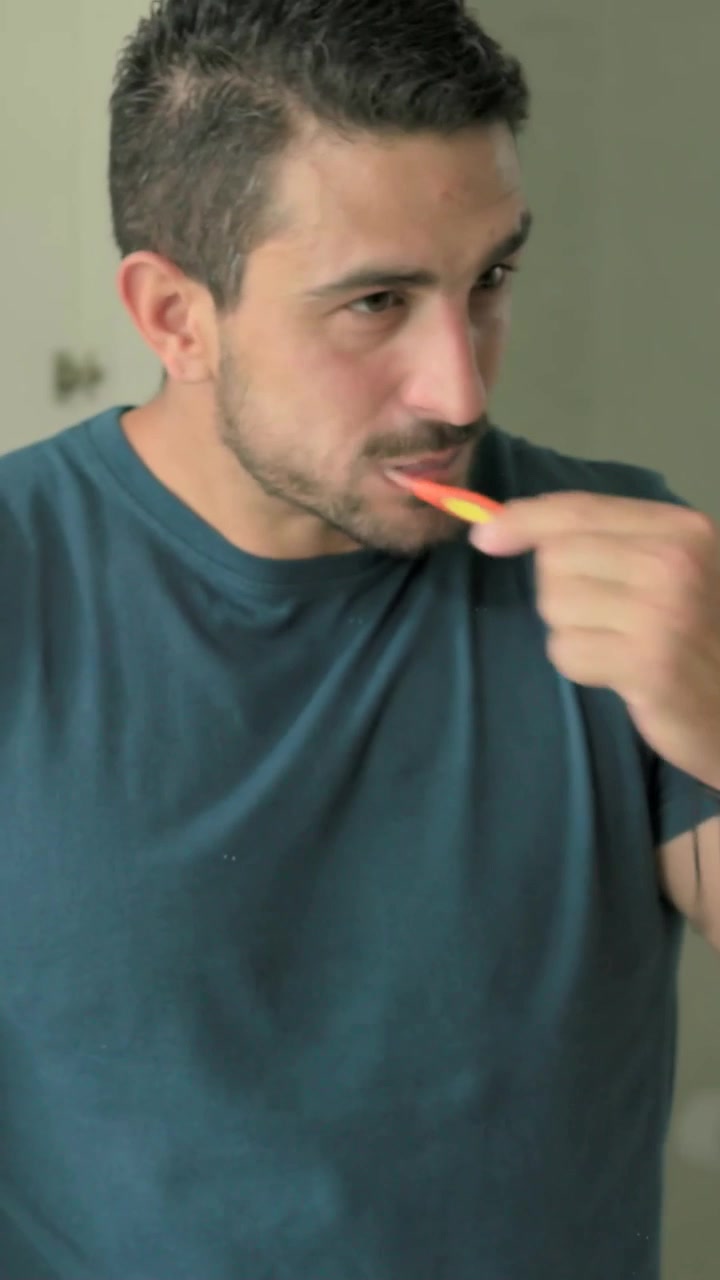 Vertical video: Bringing orange brush, man cleaning teeth at sink with foam on lips, teal shirt
