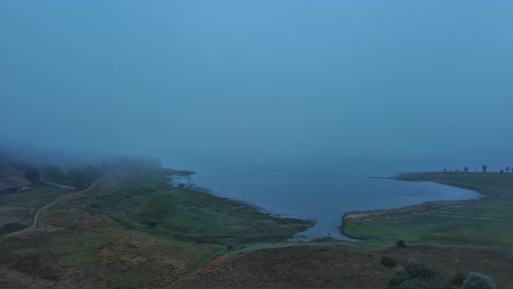 Nebliger-Morgengrauen-über-Nanclares-De-Gamboa-Mit-Einem-Ruhigen-See-Und-Einem-Verschlafenen-Dorf,-Baskenland,-Spanien,-Luftaufnahme