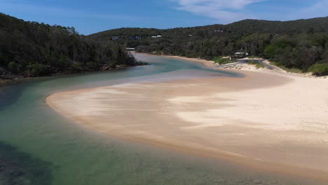 tiro de dron giratorio del arroyo korogoro y las montañas costeras con arena que sopla viento a través de una barra de arena en la cabeza del sombrero nueva gales del sur, australia