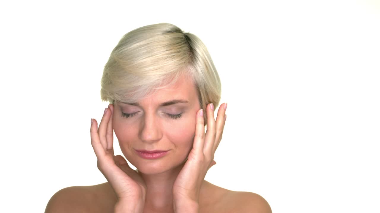 Studio portrait of a beautiful and attractive blond woman gently touching her face. Expressive clip in slow motion