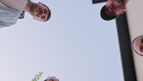bottom view of a happy group of young friends looking down and hugging during their party and relaxation in the backyard