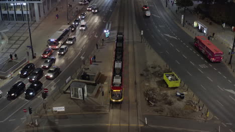 Vista-De-ángulo-Alto-Del-Tranvía-Parado-Y-Dando-Paso-A-Otros-Vehículos-En-La-Intersección.-Incline-Hacia-Arriba-La-Revelación-De-Una-Calle-Ancha-Y-Concurrida-De-Varios-Carriles-Por-La-Noche.-Varsovia,-Polonia