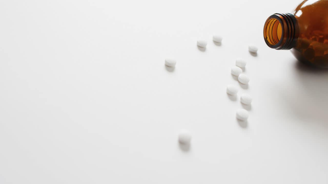 video de una botella marrón derramando píldoras blancas sobre un fondo blanco con espacio para copiar