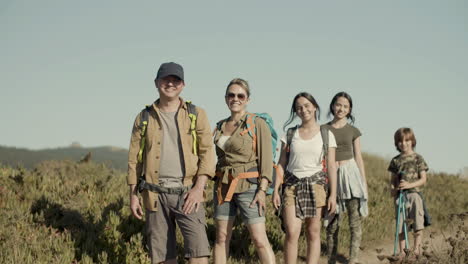 familia caucásica haciendo senderismo en un día soleado, de pie en fila y sonriendo a la cámara