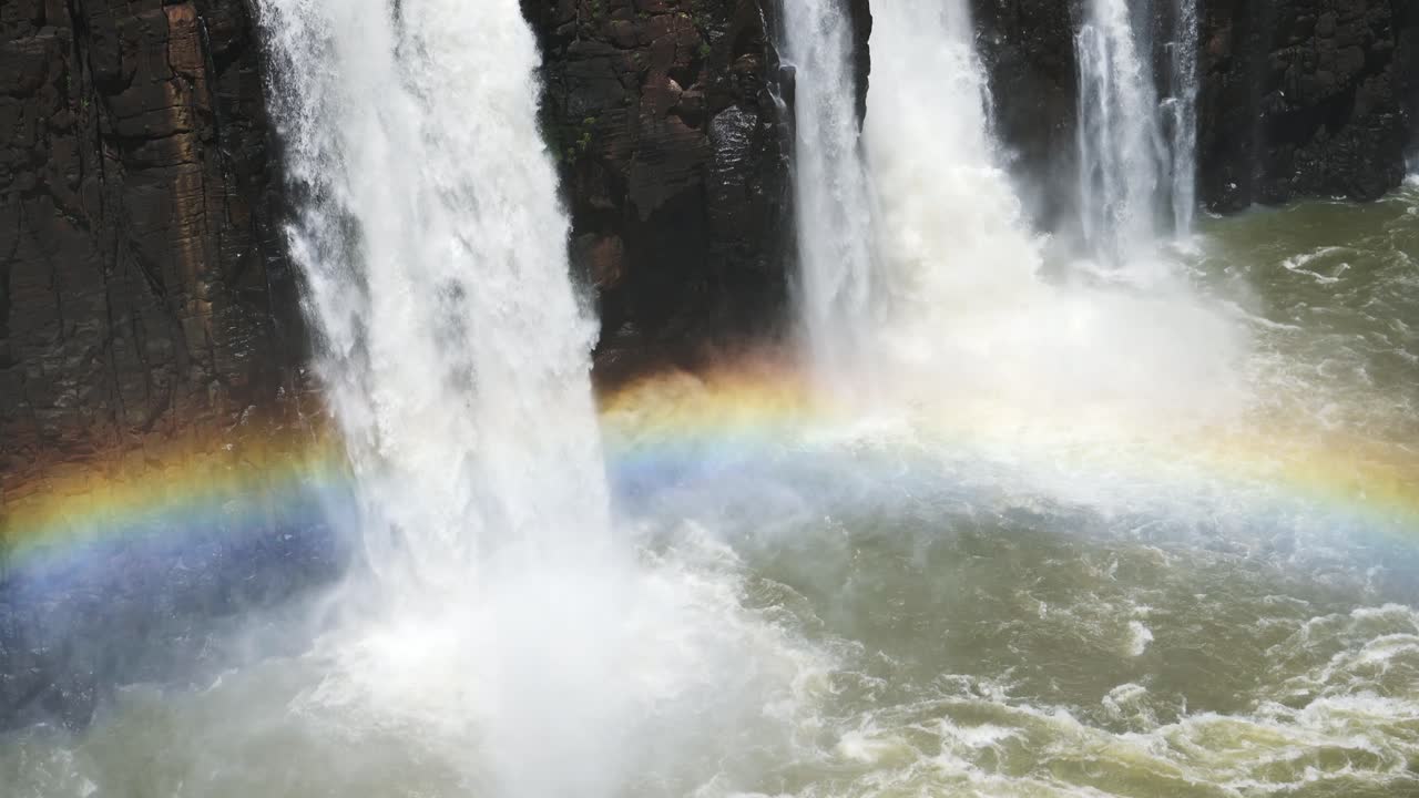 brillantes y hermosos arco iris cubiertos por enormes cascadas en cámara lenta en las cataratas de iguacu, el agua que cae del borde de un acantilado rocoso oscuro en un colorido arcoíris en las cateratas de iguazu, brasil