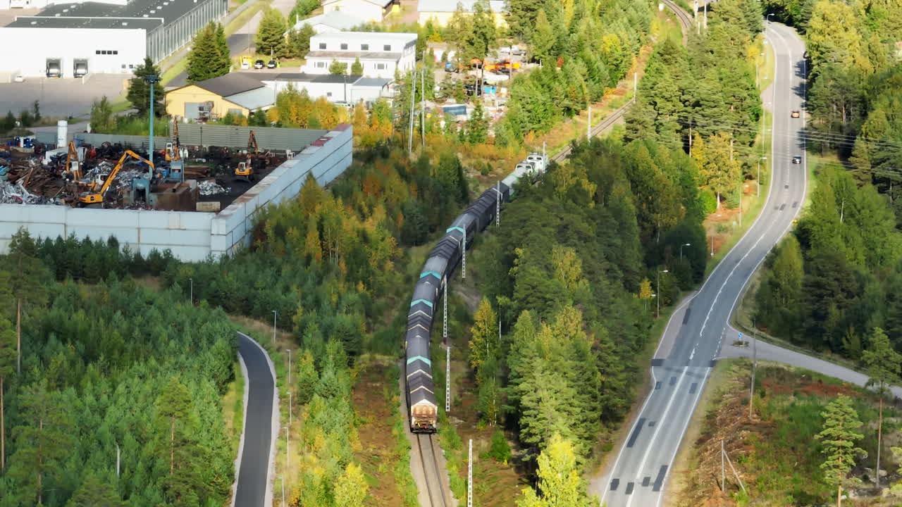 Telephoto drone shot following a cargo train in fall colors of a industrail area