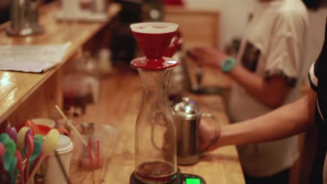 drops of freshly made coffee drip into a glass jar on a wooden table