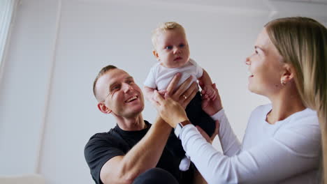 smiling caucasian dad kisses his adorable blond infant son. loving parents lift their beautiful baby up. low angle view.