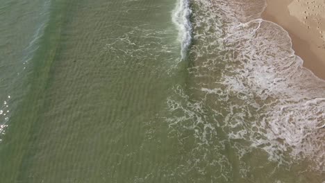 Drohnenschwenkaufnahme-Kleiner-Wellen,-Die-Am-Weißen-Sandstrand-Mit-Klarem-Wasser-Brechen