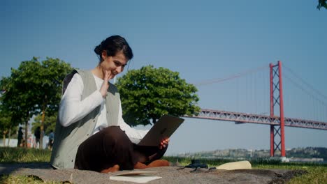 woman working on laptop in park by the bridge