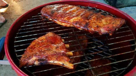 a close up shot of a man pulling ribs off the smoker with tongs after pulling up the lid