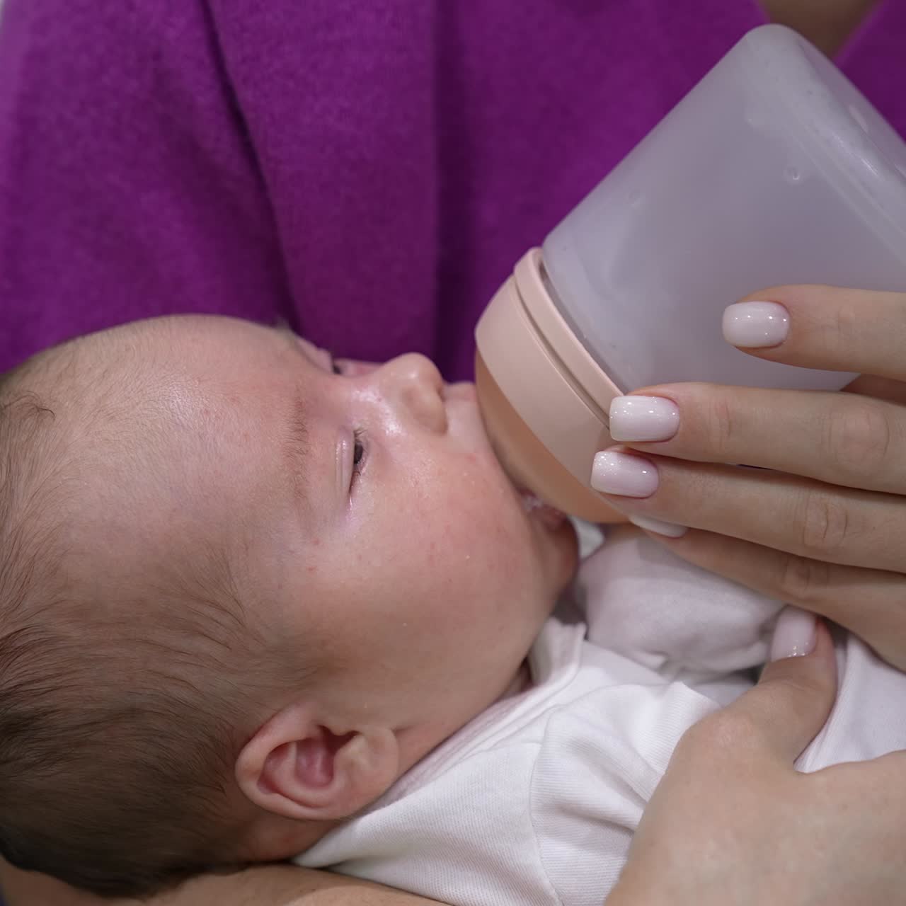 Sweet little baby eating milk from a bottle in mommy's hands. Baby finishing the bottle and lets go the bottle pacifier. Suckling baby close up