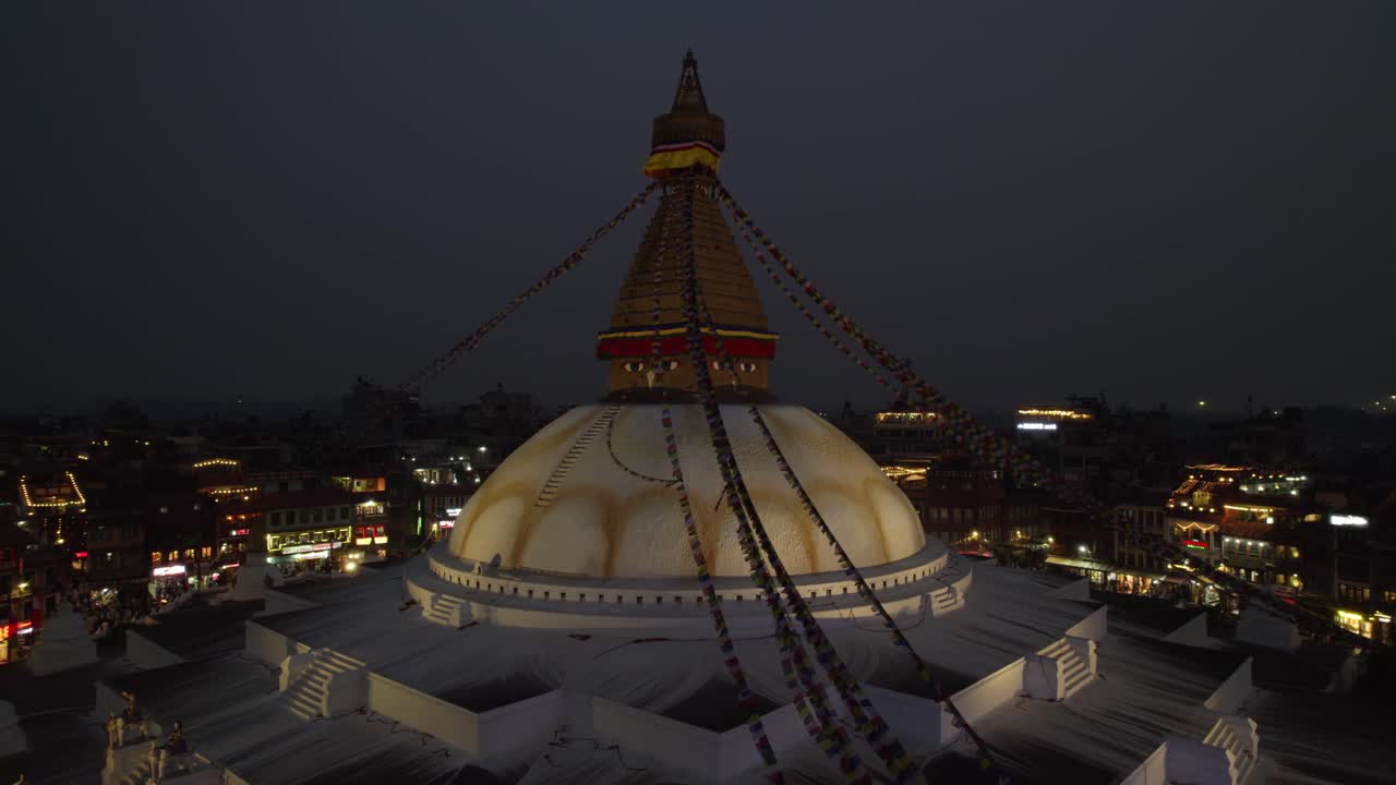 A serene night drone view of Boudhanath Stupa in Kathmandu, glowing with soft lights above the city. The sacred Buddhist monument stands out as a calm spiritual landmark against the urban nightscape