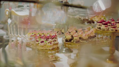 Close-up-shot-with-gold-cake-stands-filled-with-multiple-cupcakes-strawberries,-tracking-shot