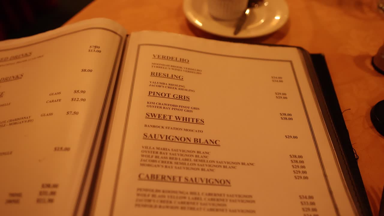 Hand flips through drink and wine menu under warm lighting at restaurant table, close-up view
