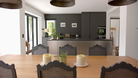 a modern kitchen with dark cabinetry is viewed from a wooden dining table