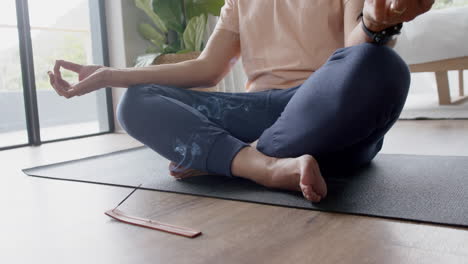 un anciano biracial practicando meditación de yoga en su casa.