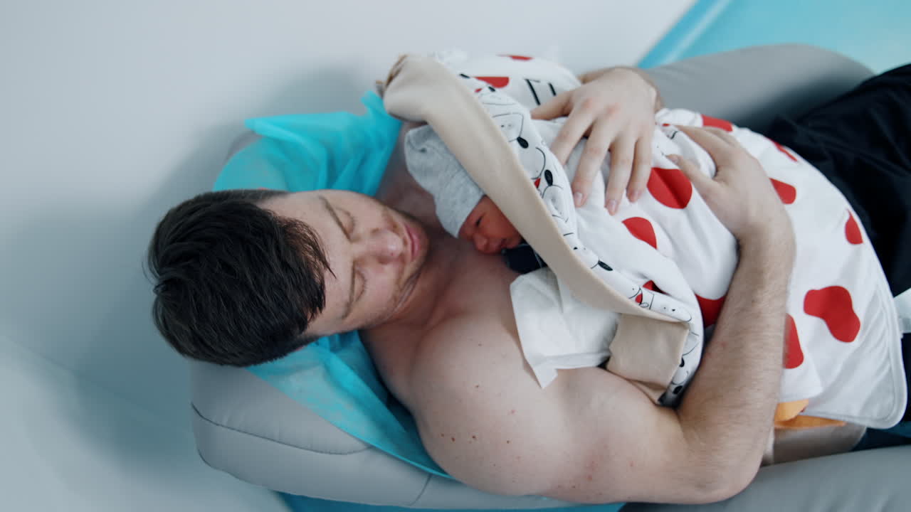 New father is holding his precious newborn child. Dad holds a baby skin to skin after birth. Top view.