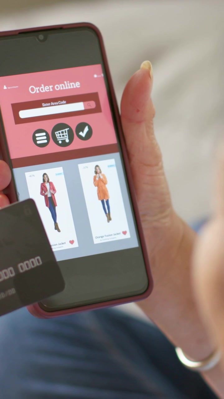 Video verticale: Donna che tiene e inclina un telefono rosso con un'app di shopping a casa, avvicinando la carta per il pagamento.