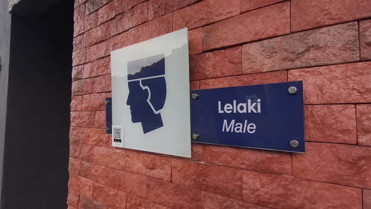 Papan tanda yang jelas untuk mushola umum terpasang di dinding. Papan tersebut menampilkan grafis pria atau wanita dengan teks dalam bahasa Melayu dan Inggris. Tanda-tanda tersebut mudah terlihat oleh publik.