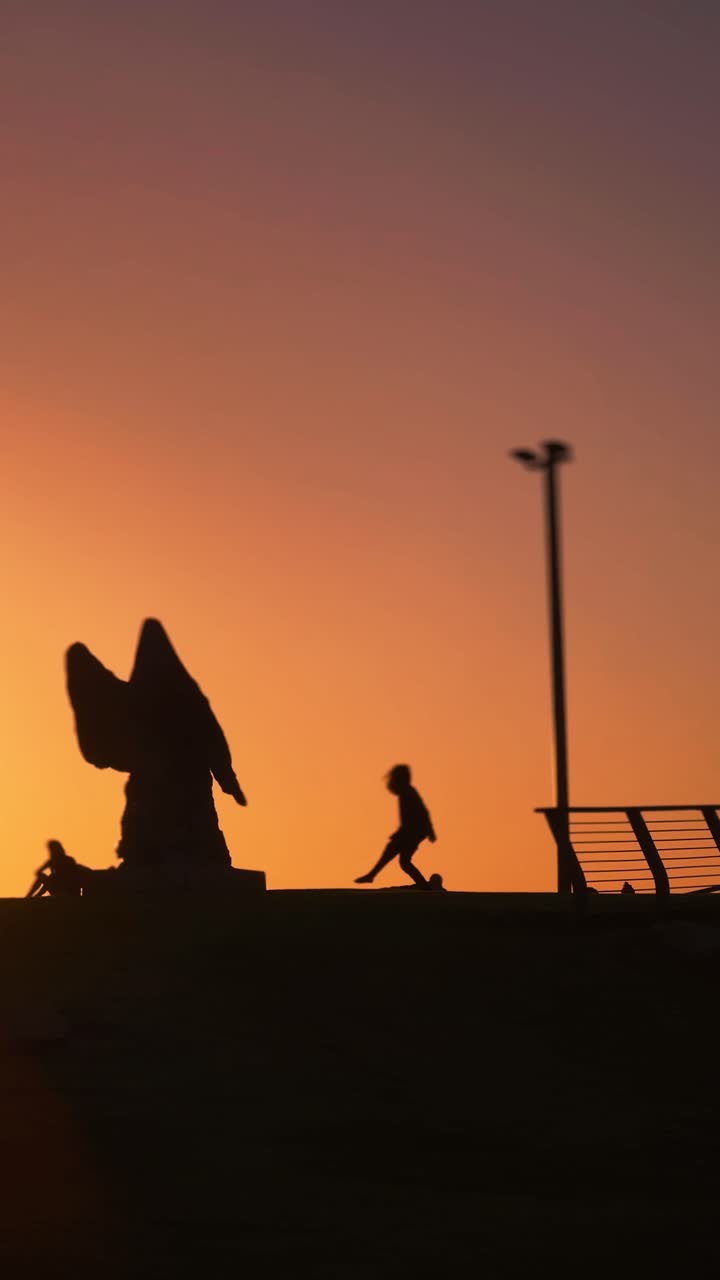 Silhouette at sunset of a person dancing in front of a statue