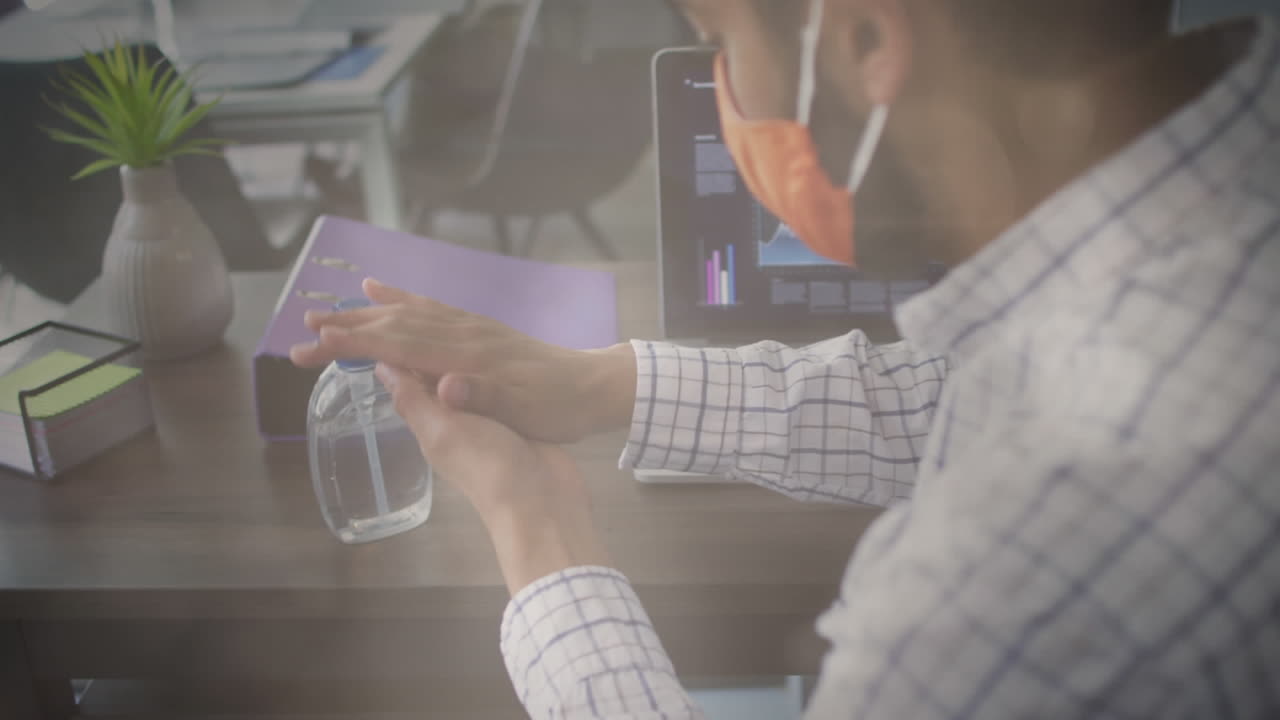 얼굴 마스크를 쓴 남자가 사무실에서 손을 소독하는 것에 대한 빛의 반점