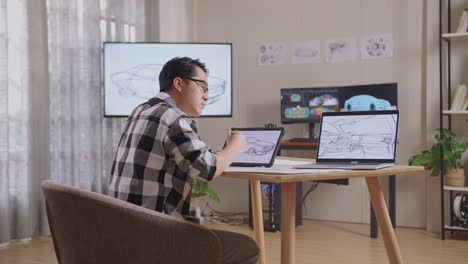 side view of asian male thinking about new car concept then raising index finger while drawing on tablet in the studio with tv and computers display 3d electric car model