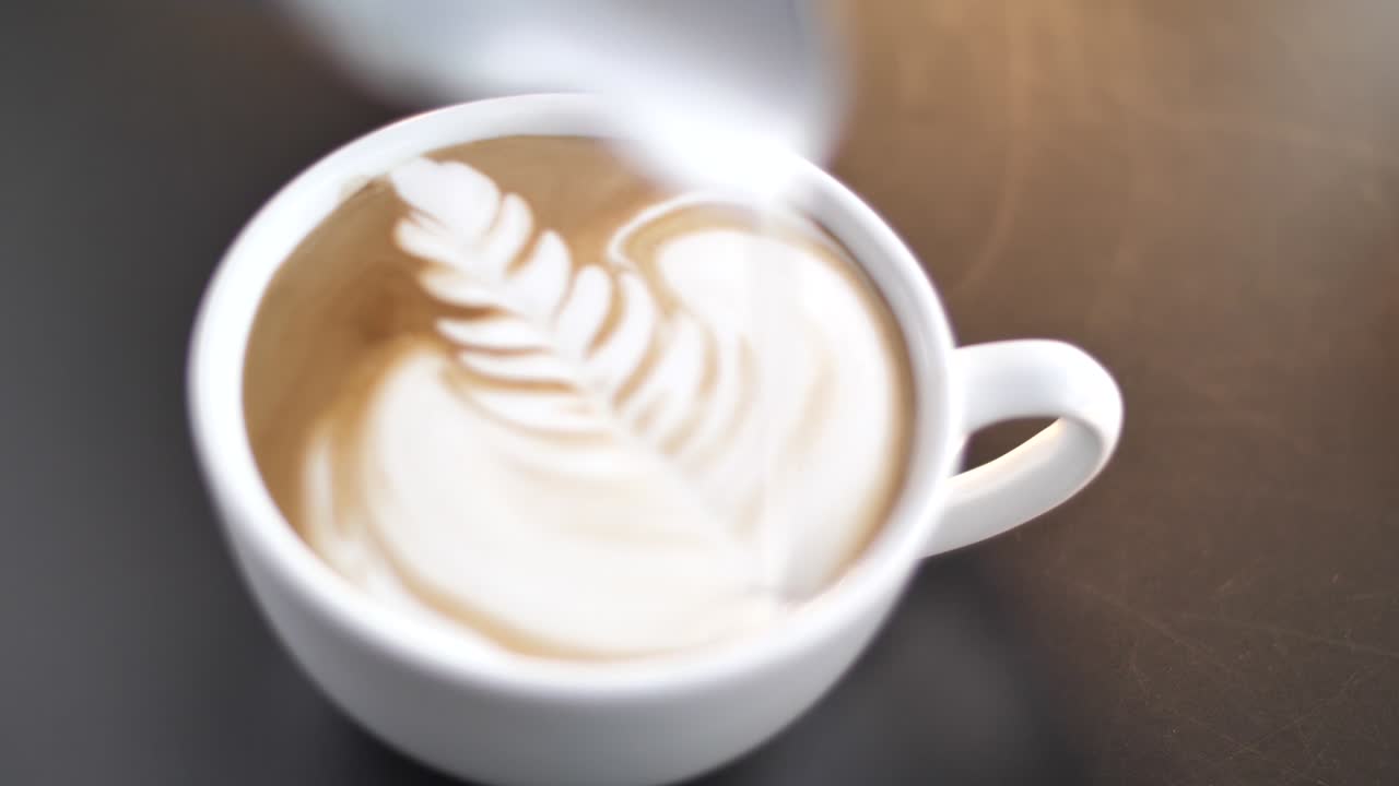 Professional barista pouring milk into coffee cup making latte art