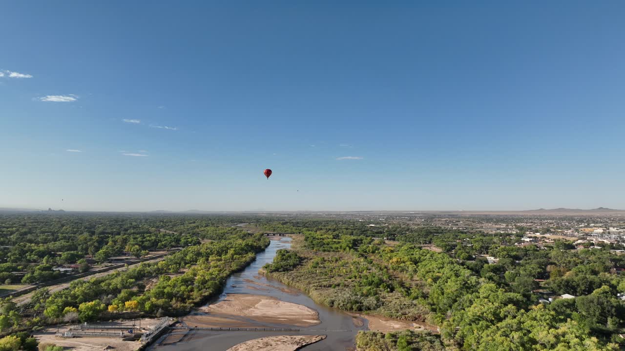 Drone POV of hot air balloons flying over stream in Albuquerque, New Mexico with clear blue skies.
