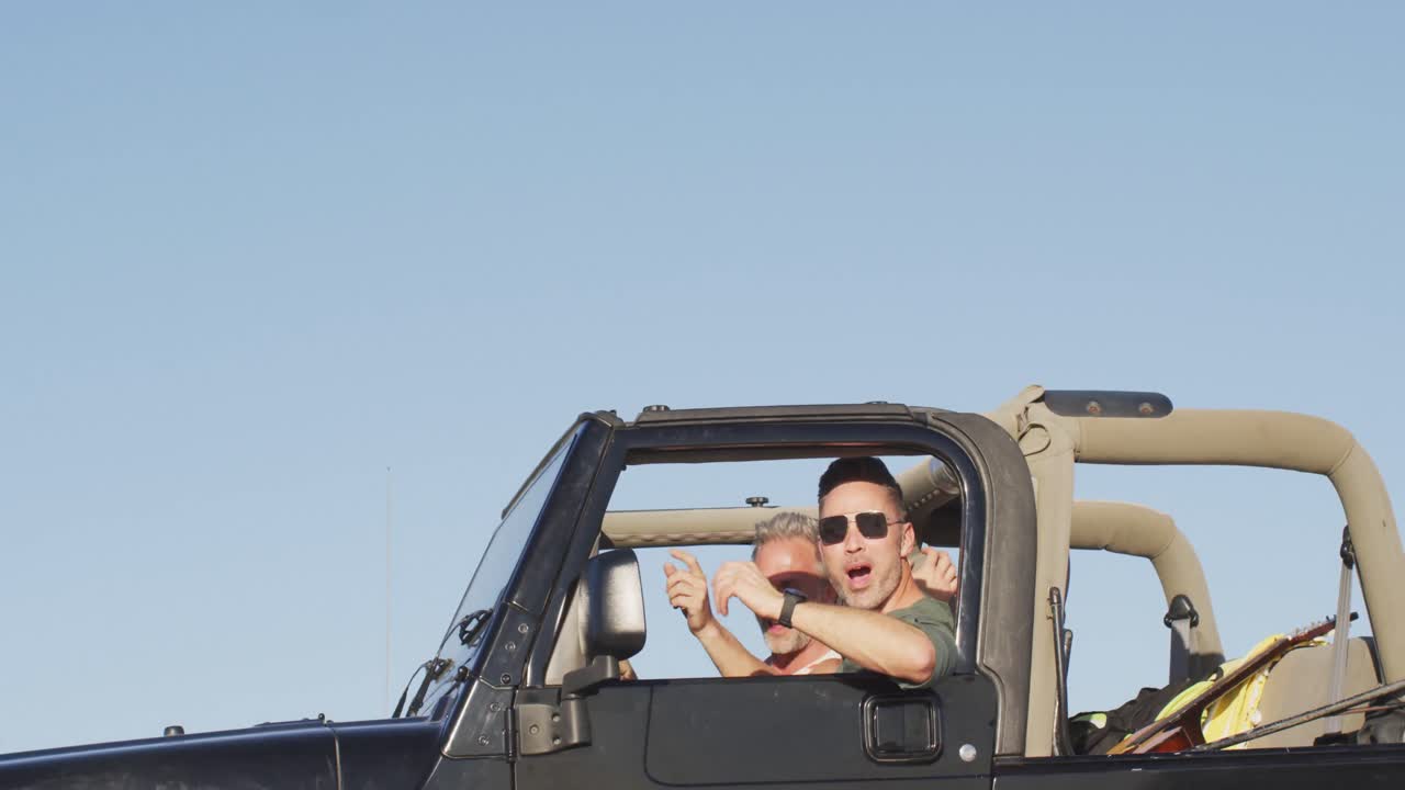 feliz pareja masculina gay caucásica en el coche admirando la vista y señalando el día soleado en la playa