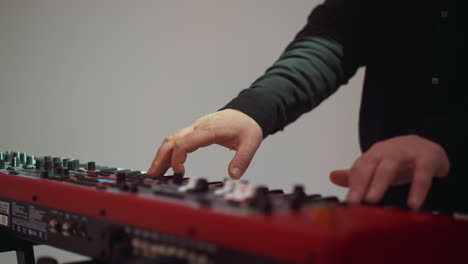 detailed view of musician's hands manipulating red electronic sampler piano knobs and keys, emphasizing technique and instrument detail against a white backdrop